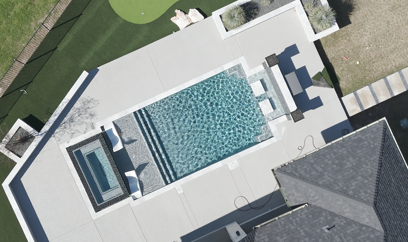 Aerial view of a custom rectangular gunite pool with raised spa, tanning ledge, and stone decking in Waldsanger