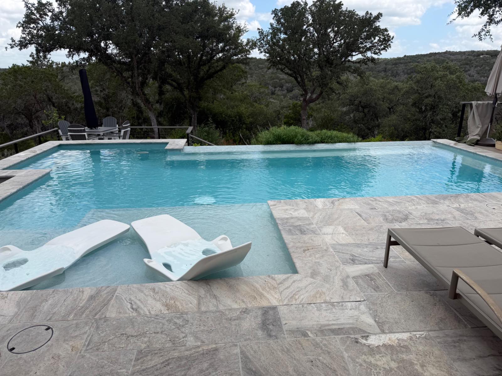 Vanishing-edge custom pool with travertine deck and sweeping Texas Hill Country views under live oaks, built by J. Oliver Pools in Boerne