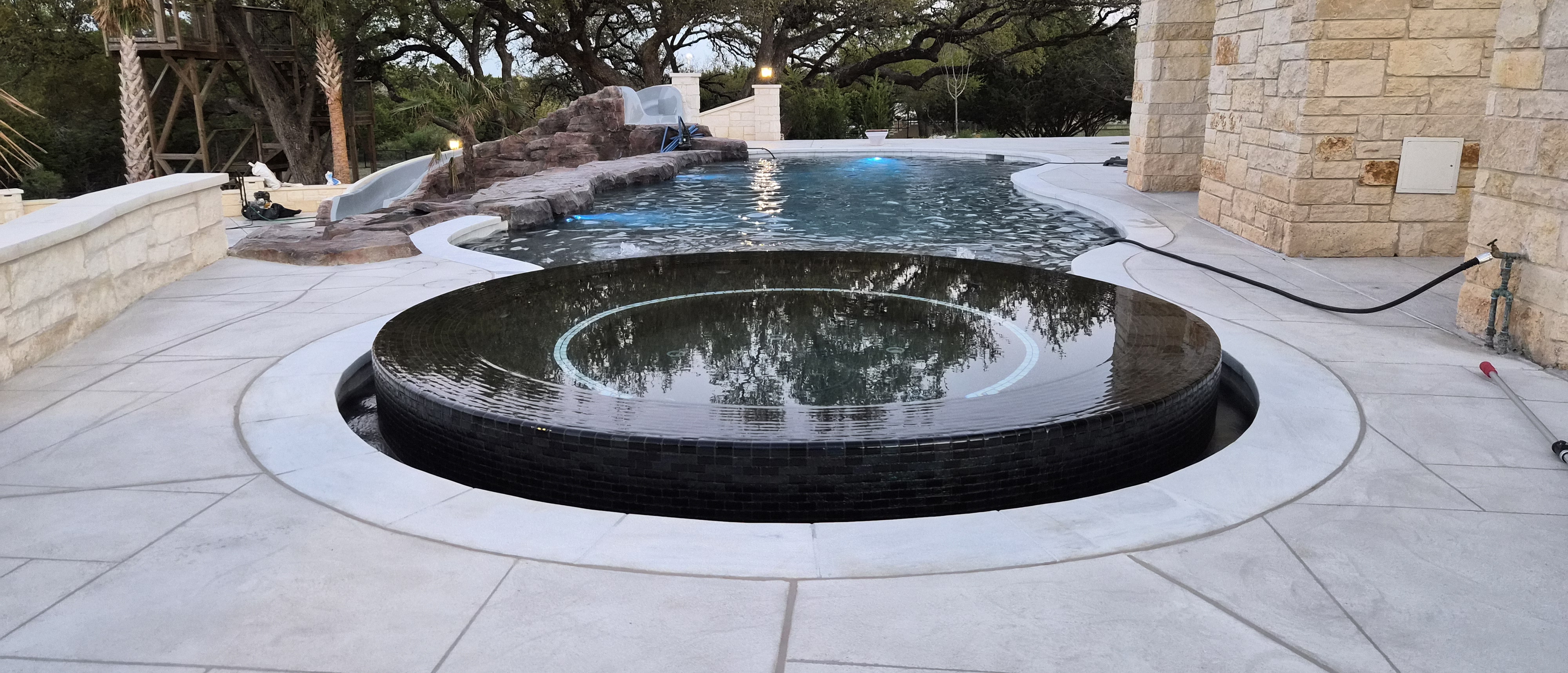 Freeform gunite pool with rock waterfall and slide at dusk in Hidden Trails