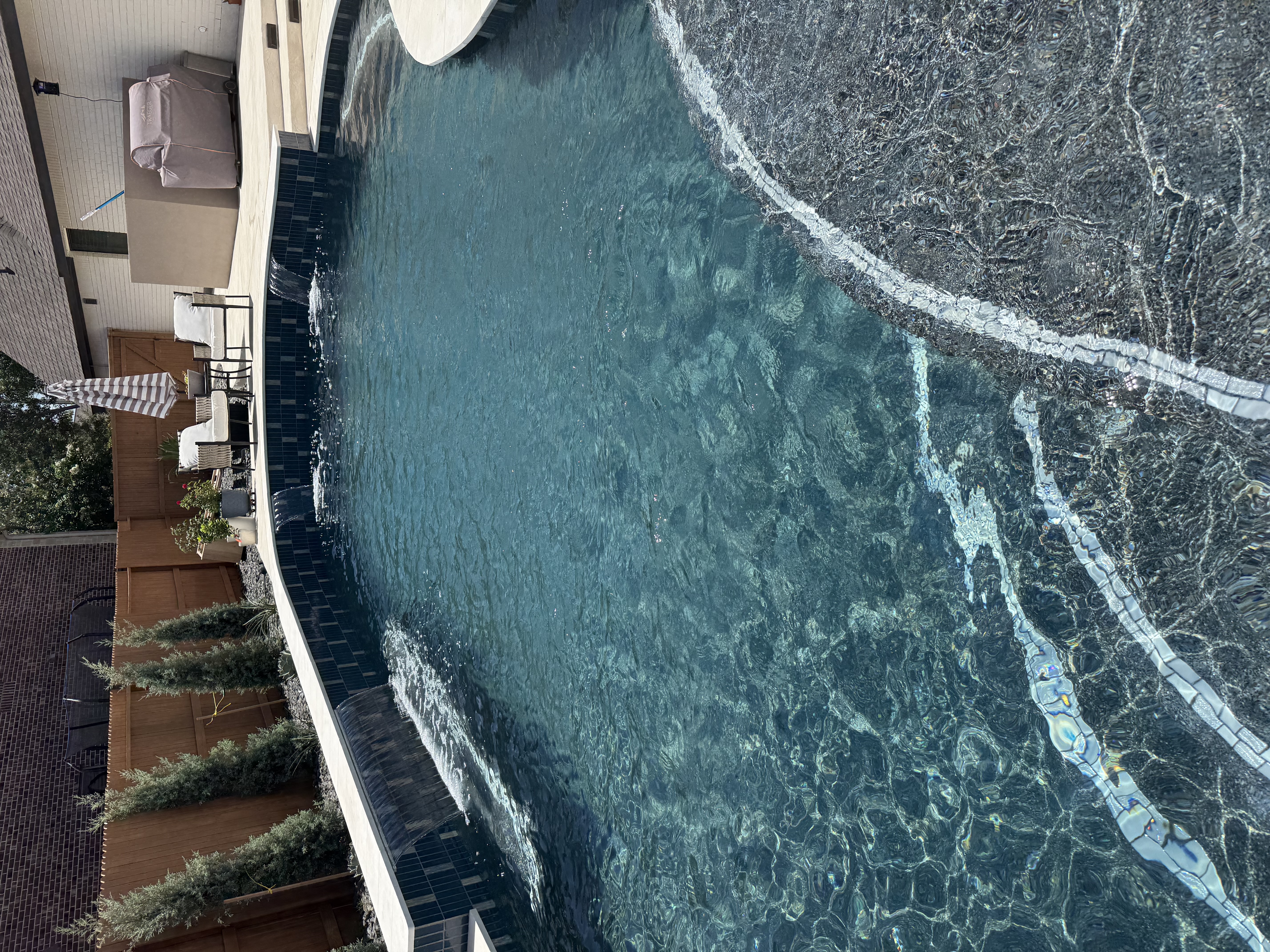 Freeform pool with twin sheer-descent water features over a dark-blue glass-tile wall and PebbleTec interior in the Veramendi community of New Braunfels