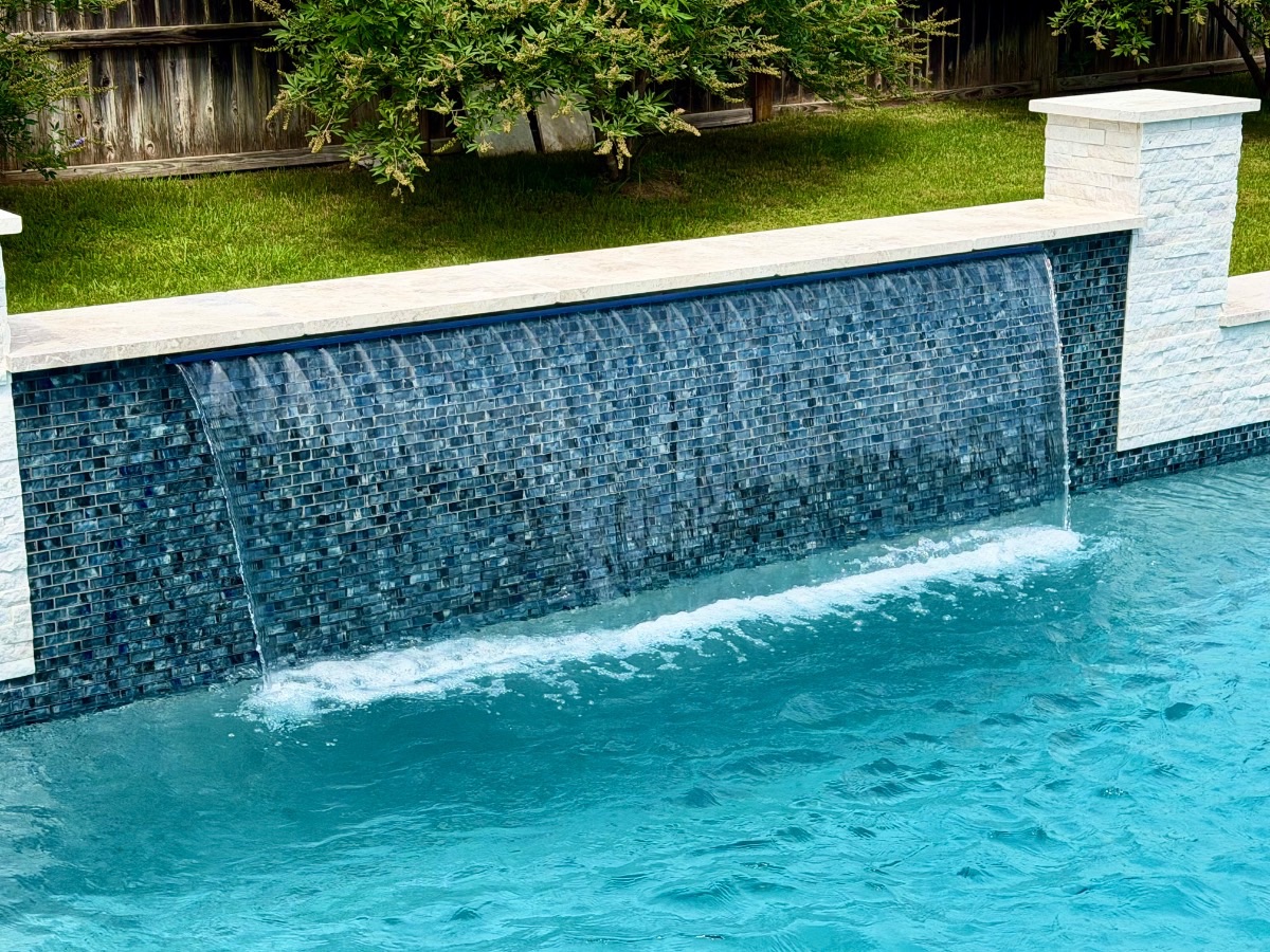 Close-up of a glass-tile sheer-descent waterfall spilling over a deep-blue mosaic wall capped with white limestone in New Braunfels