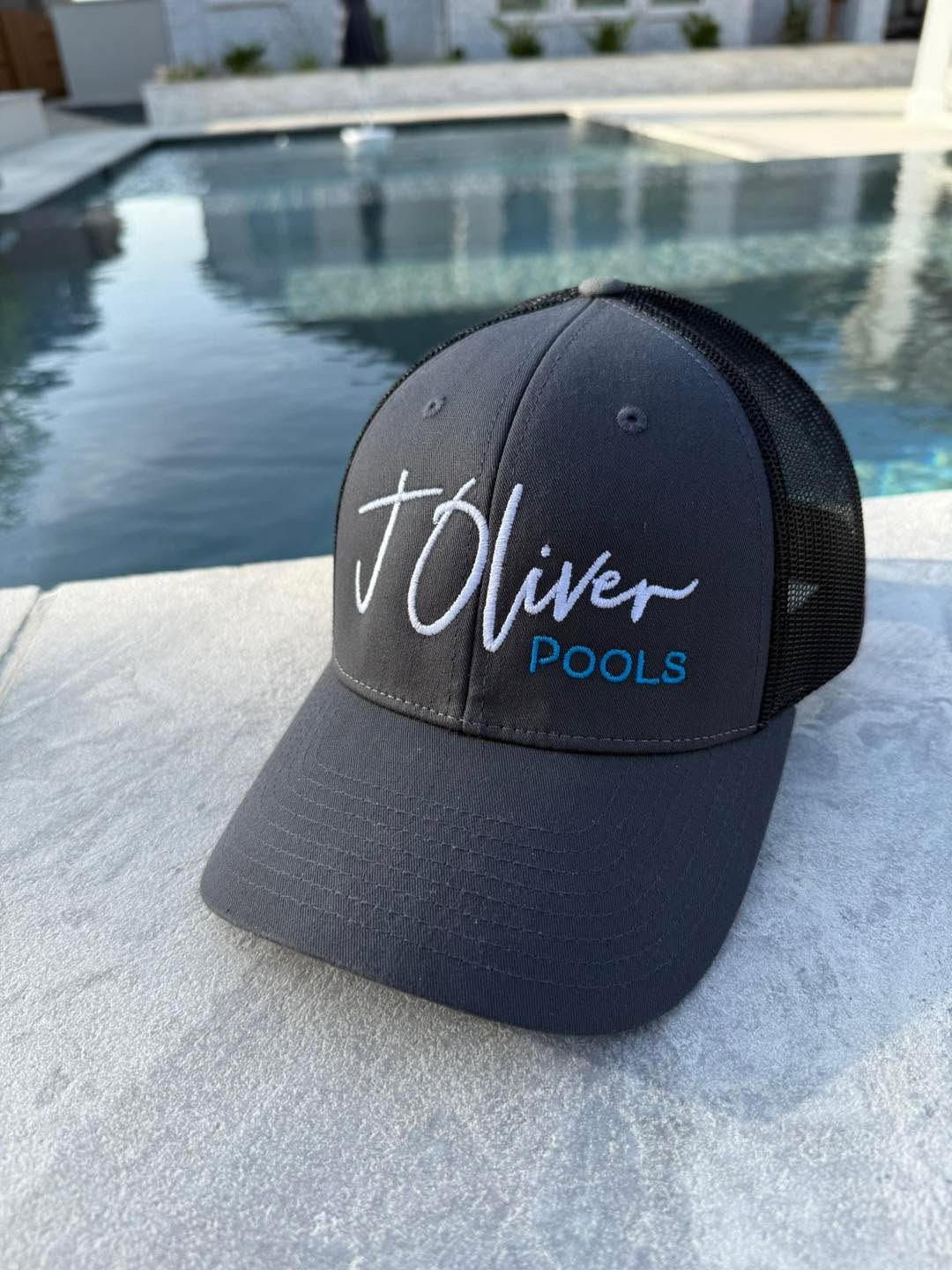 J. Oliver Pools branded cap resting poolside on new travertine coping