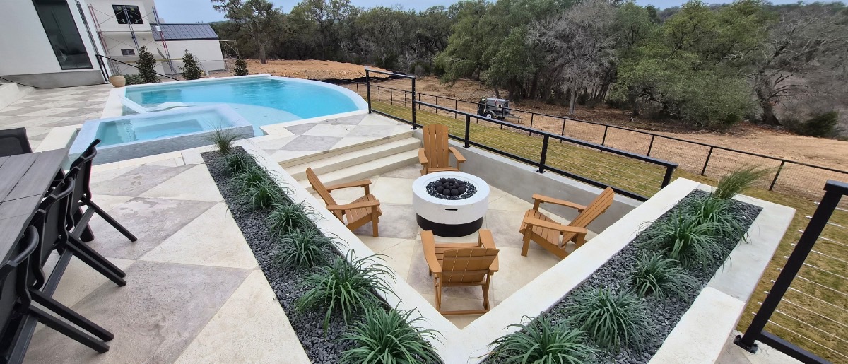 After construction: completed freeform pool with raised spa, custom cut-stone diamond-pattern decking, and a sunken fire pit lounge with adirondack chairs, New Braunfels