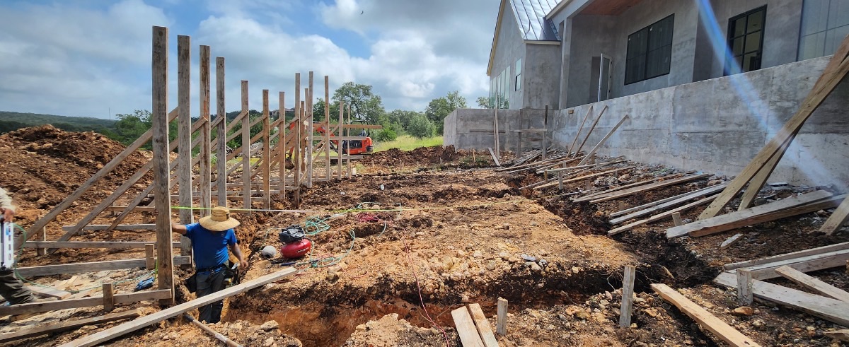 Before construction: graded dirt hillside behind a New Braunfels home, framed with temporary wood layout stakes