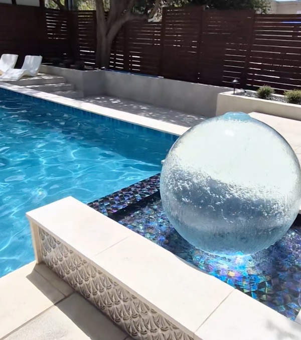 PAL WaterSphere bubbler orb churning with water beside a custom pool with iridescent glass tile, built by J. Oliver Pools near New Braunfels, Texas