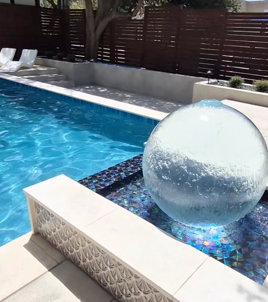 PAL WaterSphere bubbler orb churning with water beside a custom pool with iridescent glass tile, built by J. Oliver Pools near New Braunfels, Texas