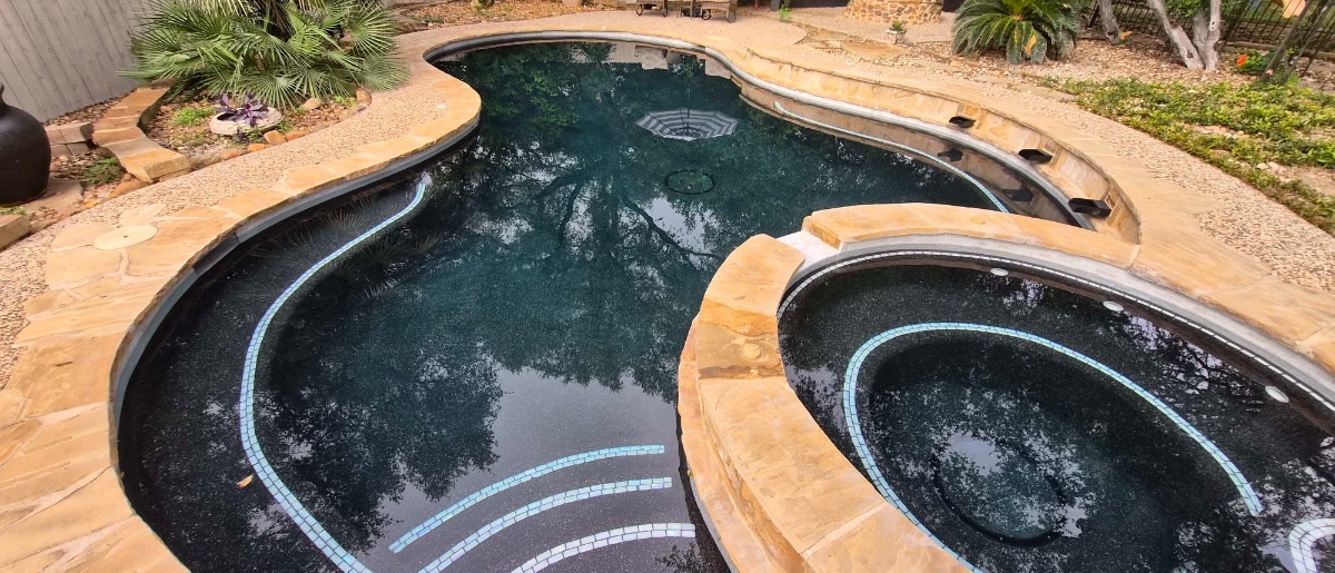 After renovation: same freeform pool and spa refinished in a midnight Pebble interior with iridescent glass-tile step and spa accents, San Antonio