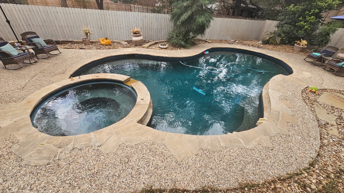 Before renovation: aging freeform pool and round spa with dated plaster, dark water, and flagstone coping in the Woodlands of Camino Real, San Antonio