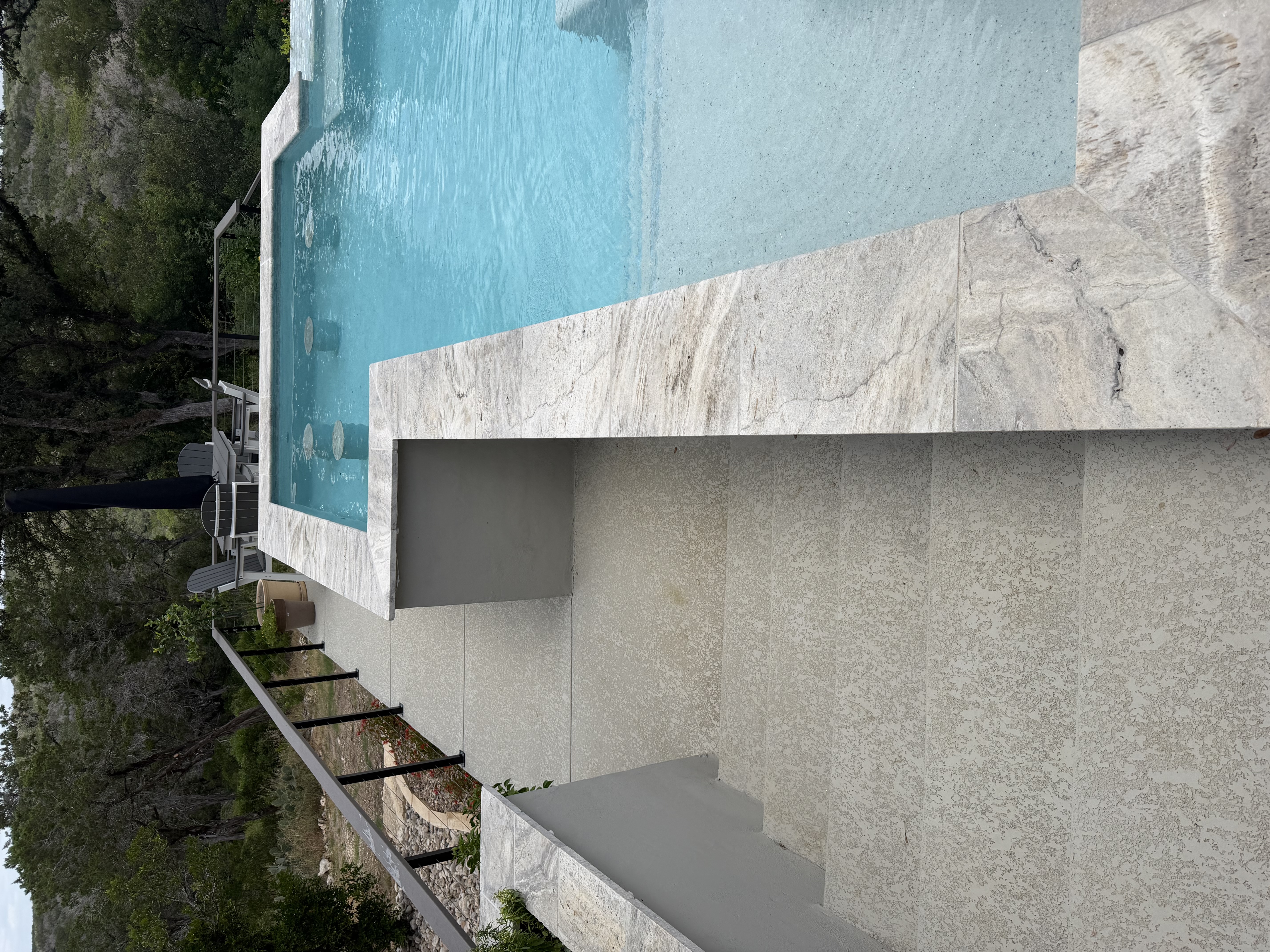 Raised travertine sun shelf and lounge deck overlooking a vanishing-edge pool and Texas Hill Country views