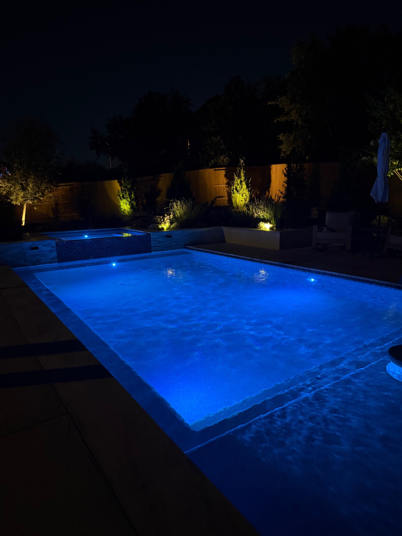 Renovated pool at night glowing blue with new LED lighting and illuminated raised spa and landscaping