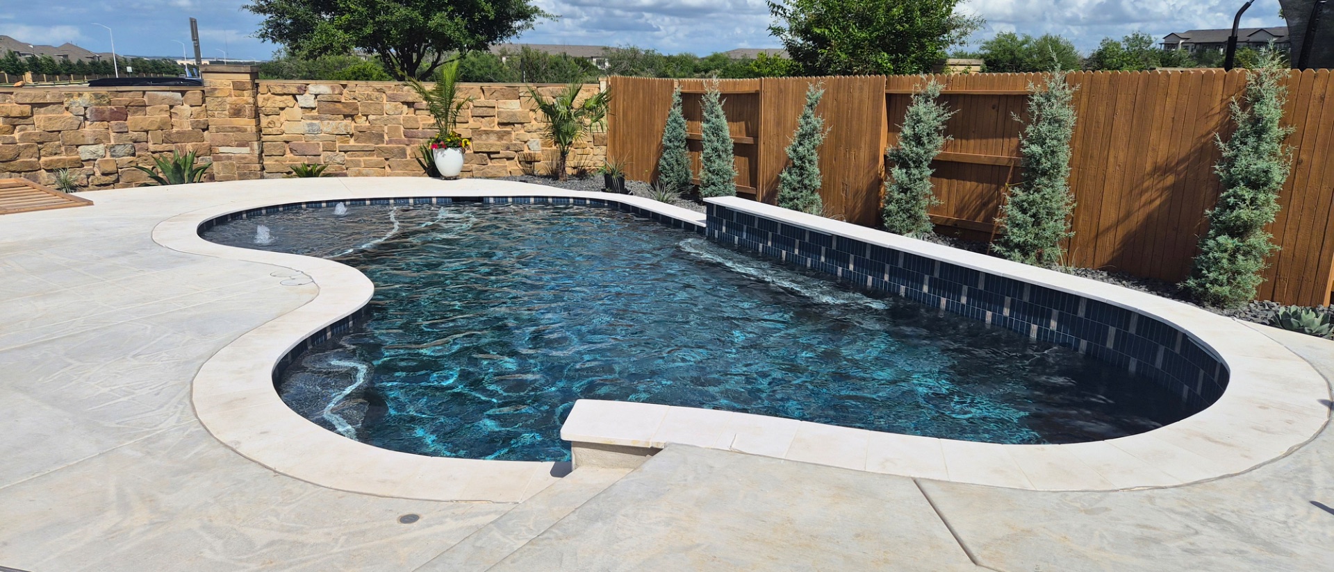 Custom freeform gunite pool with tanning ledge and raised tile spa, built by J. Oliver Pools in Spring Branch, Texas