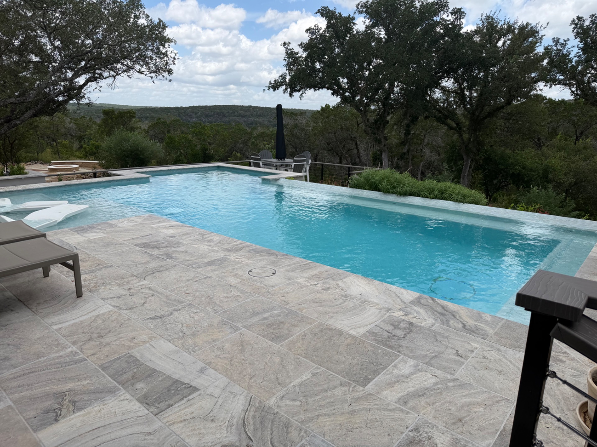 Custom infinity-edge gunite pool with travertine deck overlooking the Hill Country, built by J. Oliver Pools in Wimberley, Texas